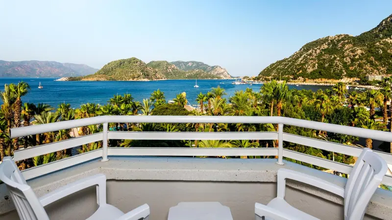Vue d'une terrasse avec des fauteuils blancs donnant sur la mer et les montagnes.