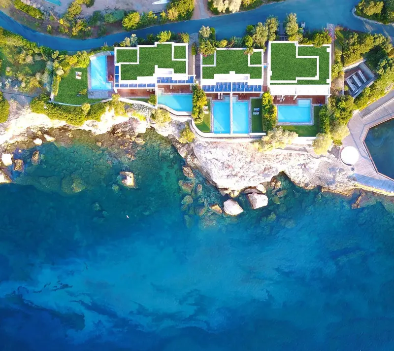 Vue aérienne d'un complexe hôtelier blanc bordant une côte rocheuse et une mer turquoise.