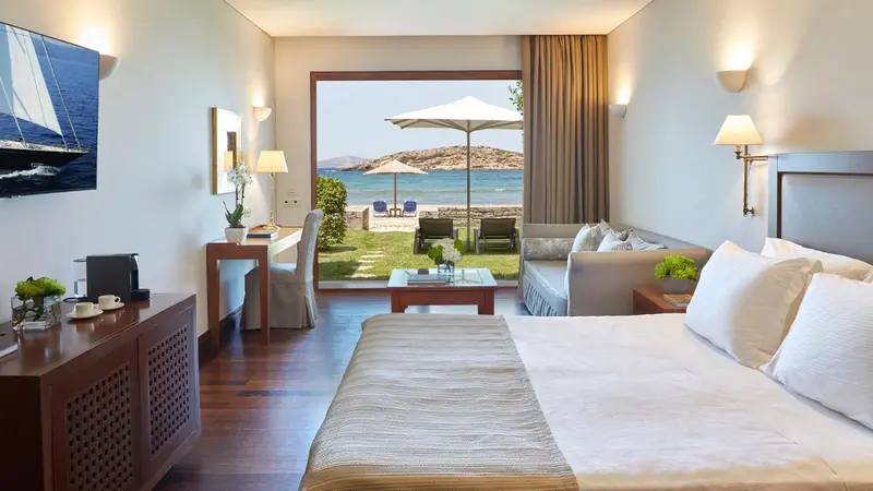 Une chambre lumineuse avec un lit et un coin salon donnant sur une vue mer.