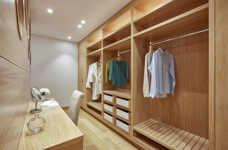 Un dressing en bois clair avec des vêtements suspendus et des tiroirs.