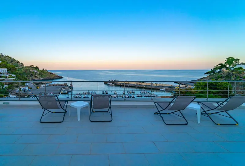 Terrasse avec chaises longues donnant sur la mer au coucher du soleil.