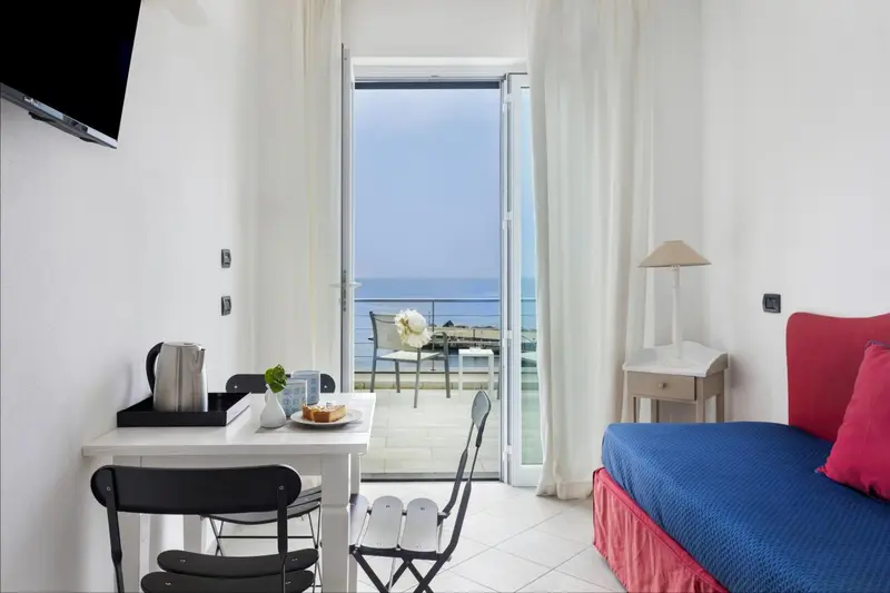 Une chambre lumineuse s'ouvre sur une terrasse avec vue sur la mer.