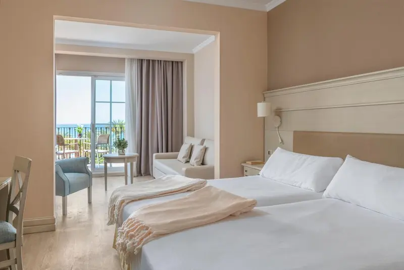 Une chambre lumineuse avec un lit double et un coin salon donnant sur une terrasse.
