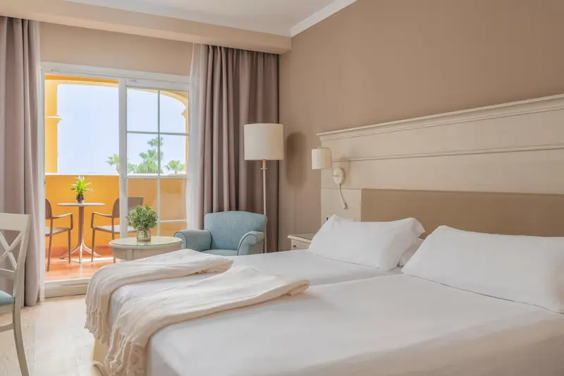 Une chambre lumineuse avec un lit blanc et un accès à un balcon.