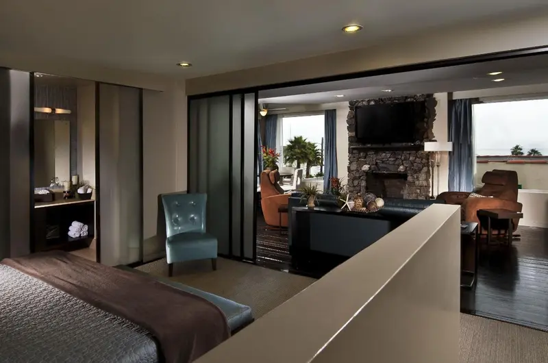 Une chambre spacieuse s'ouvre sur un salon avec cheminée et vue sur l'extérieur.