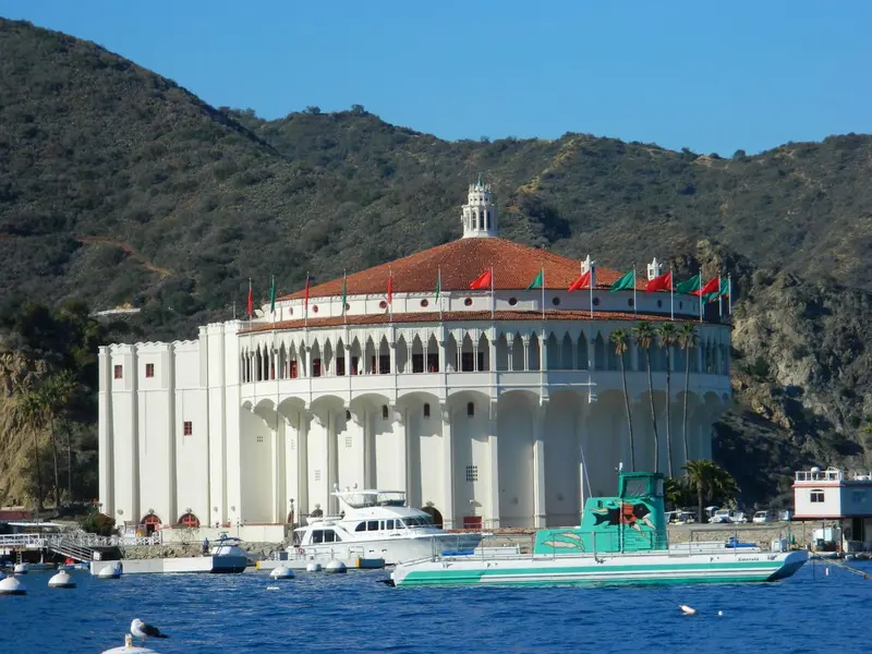 Bâtiment blanc à toit rouge bordant une côte rocheuse et une marina.