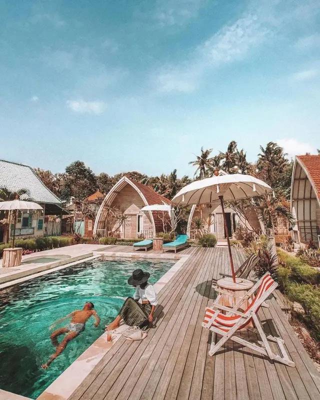 Une piscine bordée d'une terrasse en bois avec des transats et des bungalows en arrière-plan.