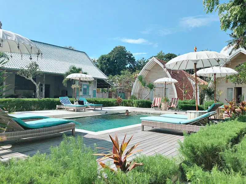 Transats turquoise bordent une piscine turquoise dans un jardin tropical.