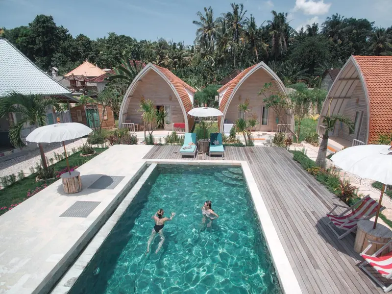 Vue aérienne d'une piscine rectangulaire entourée de bungalows aux toits en forme de vagues.