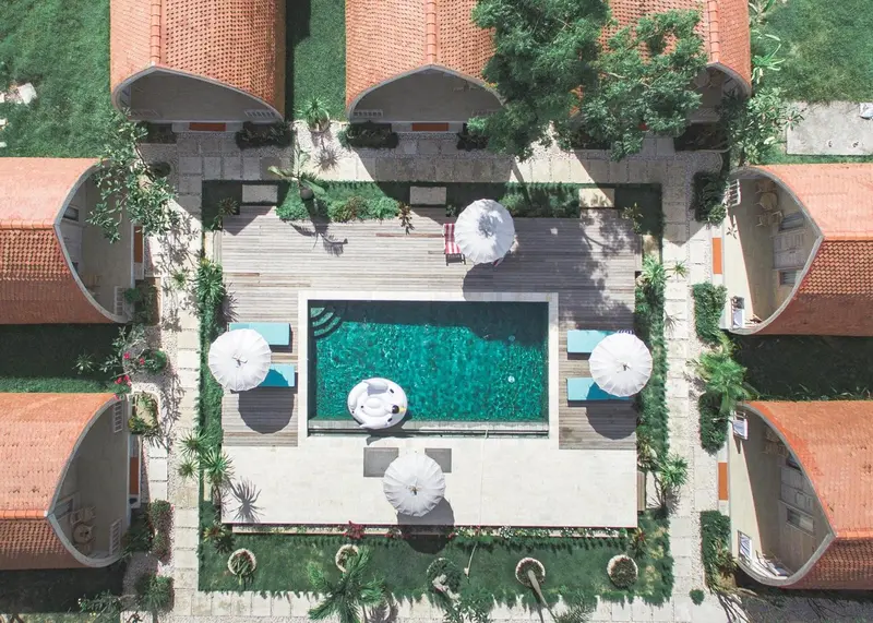 Vue aérienne d'une piscine rectangulaire entourée de bâtiments aux toits en tuiles et de transats blancs.