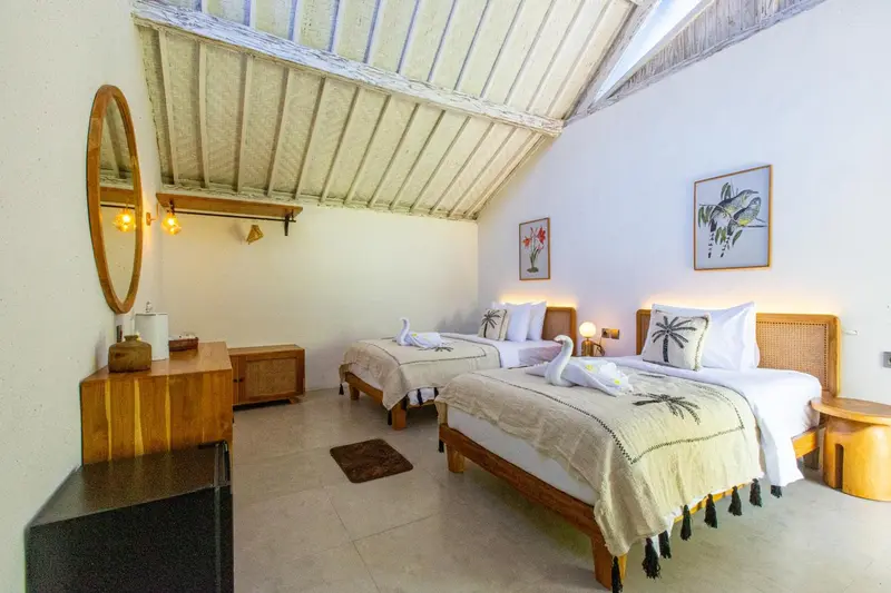 Chambre lumineuse avec deux lits simples et décoration tropicale.