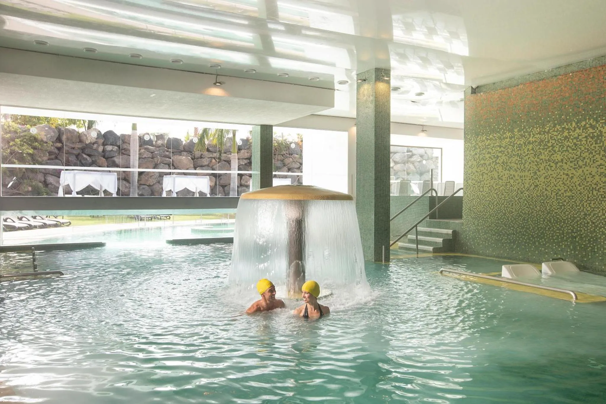 Deux personnes se détendent dans une piscine intérieure avec une cascade.