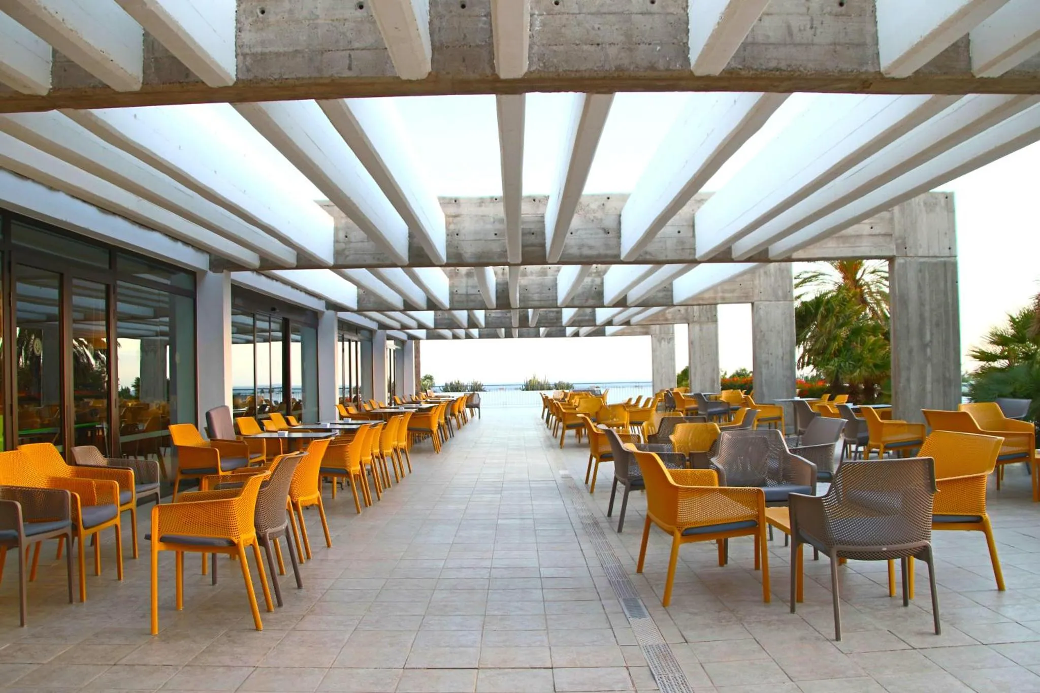 Terrasse ombragée avec tables et chaises face à la mer.