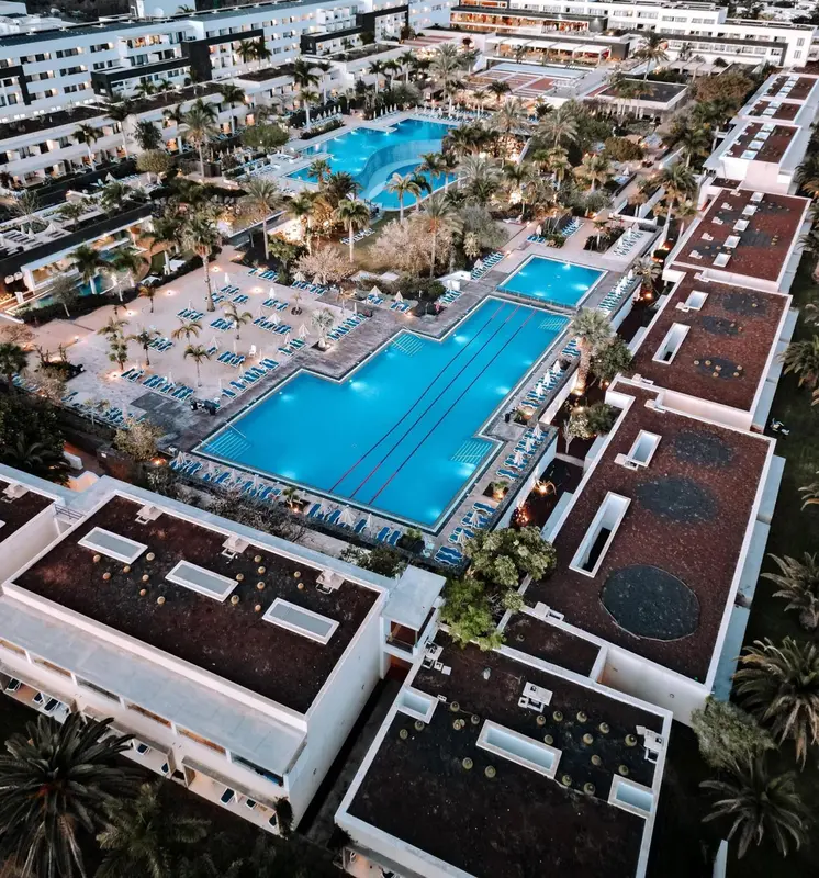 Vue aérienne d'un complexe hôtelier avec plusieurs piscines et des bâtiments blancs.