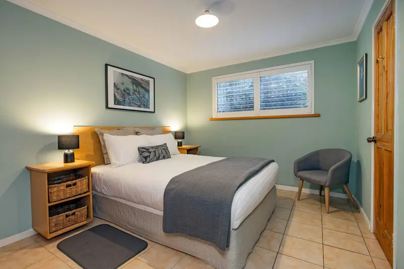 Une chambre lumineuse avec un lit double et un fauteuil.