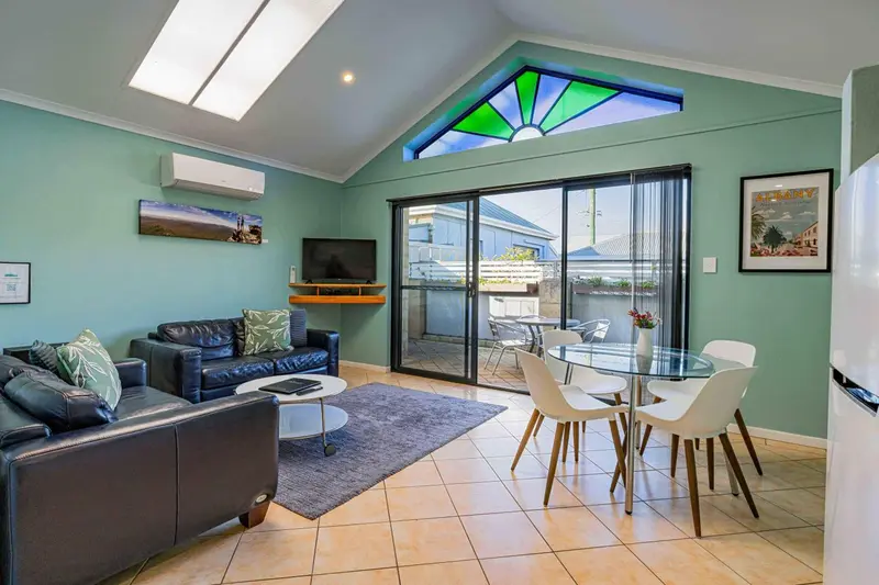 Espace de vie lumineux avec canapé, table basse et coin repas près d'une baie vitrée.