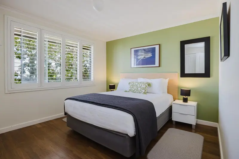 Une chambre lumineuse avec un grand lit et des fenêtres à volets.