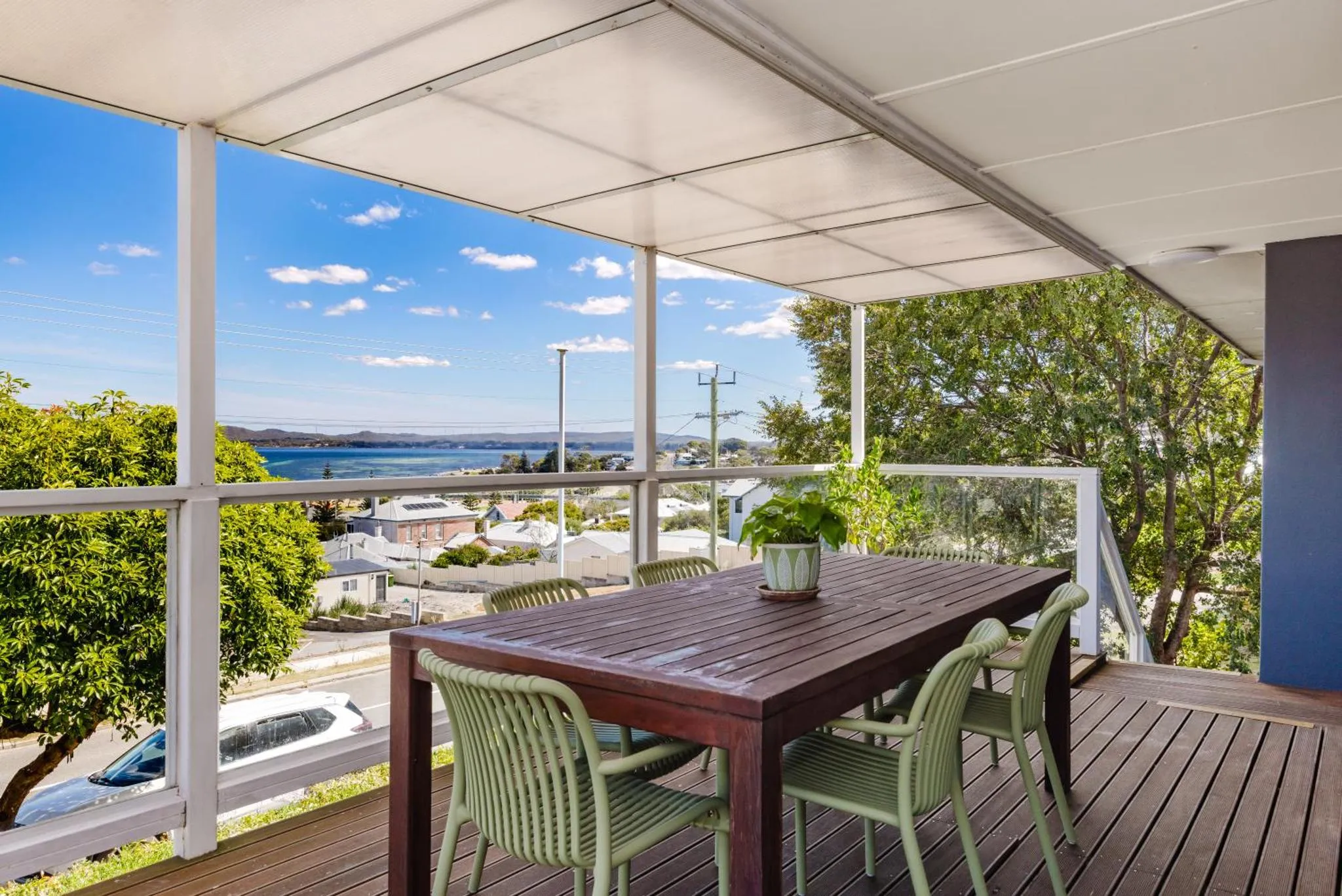 Une table et des chaises se trouvent sur une terrasse couverte avec vue sur la mer et la végétation.