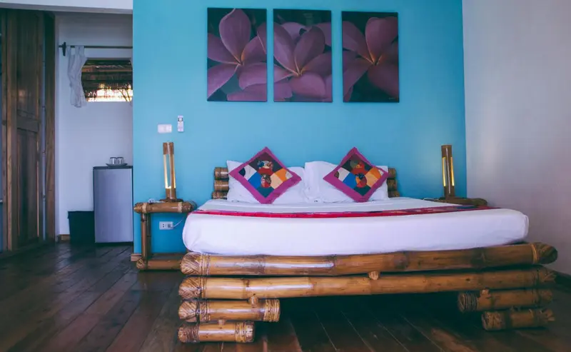 Une chambre lumineuse avec un grand lit en bambou et des tableaux floraux.