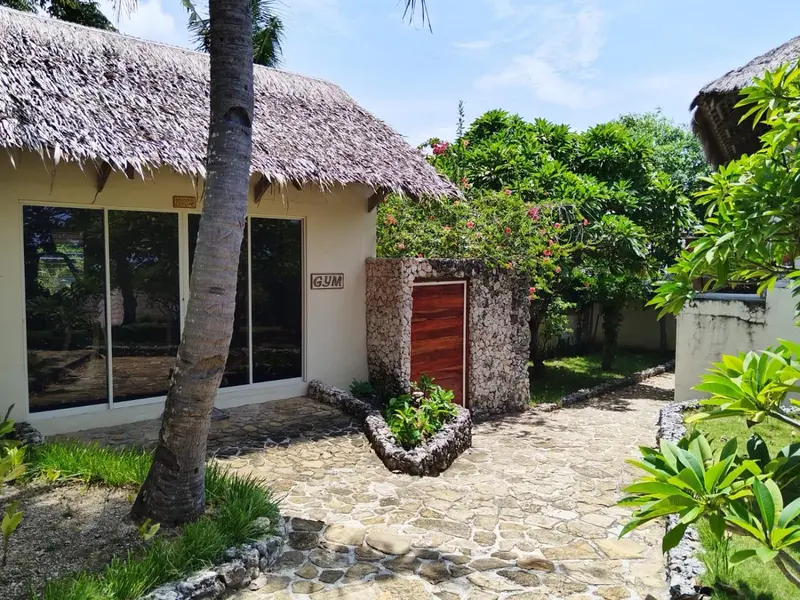 Bâtiment blanc avec toit de chaume et végétation tropicale.