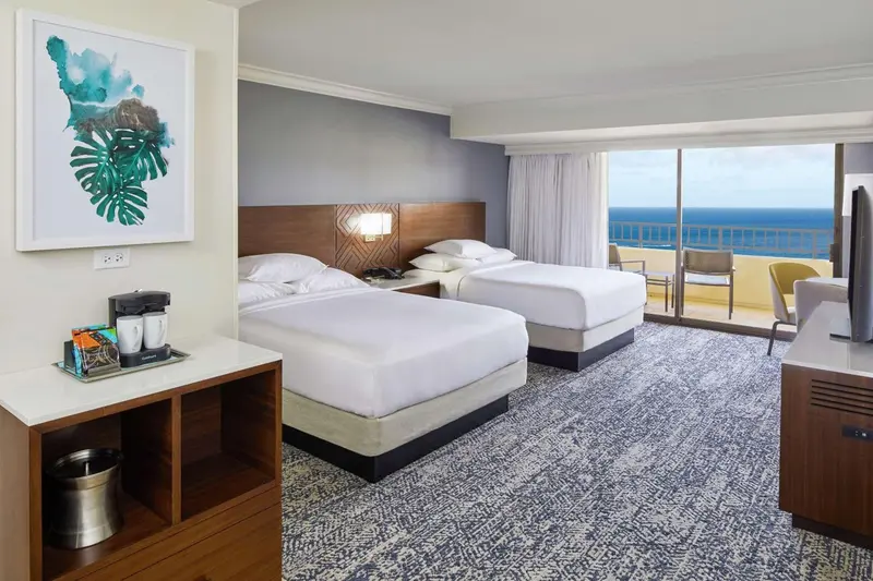 Une chambre lumineuse avec deux lits et une vue sur la mer.