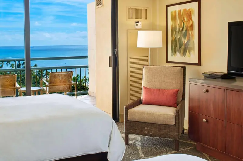 Une chambre lumineuse avec un fauteuil et une vue sur la mer depuis un balcon.
