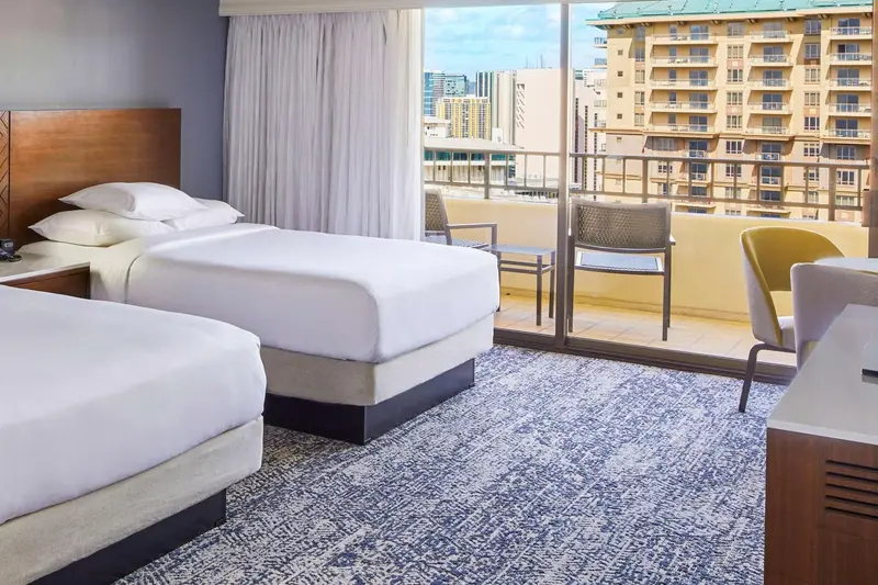 Chambre avec deux lits et balcon donnant sur la ville.