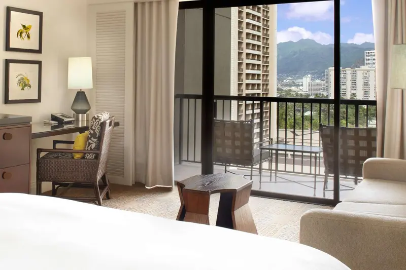 Une chambre lumineuse s'ouvre sur un balcon avec vue sur la ville et les montagnes.