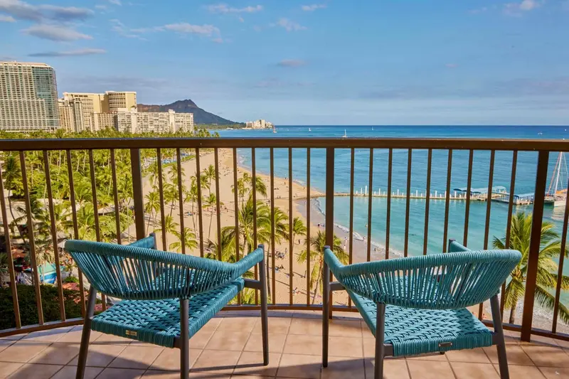 Deux fauteuils en osier sur une terrasse avec vue sur la mer et la plage.