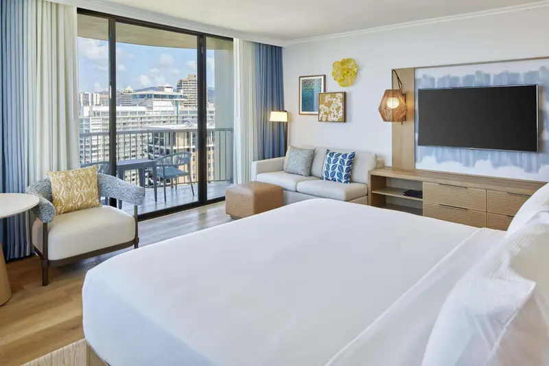 Une chambre lumineuse avec un coin salon et un balcon offrant une vue sur la ville.