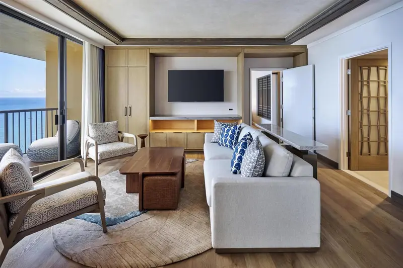 Espace de vie lumineux avec canapés et fauteuils face à une baie vitrée donnant sur la mer.