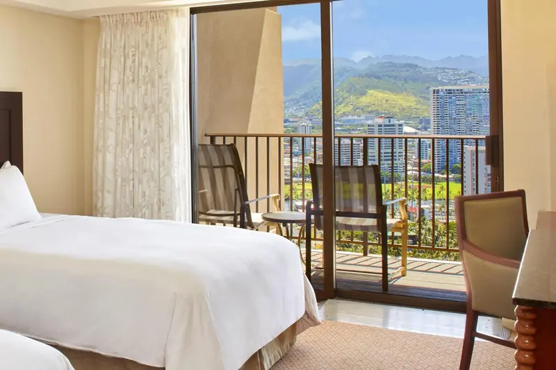 Une chambre lumineuse s'ouvre sur une terrasse avec vue sur un paysage montagneux.
