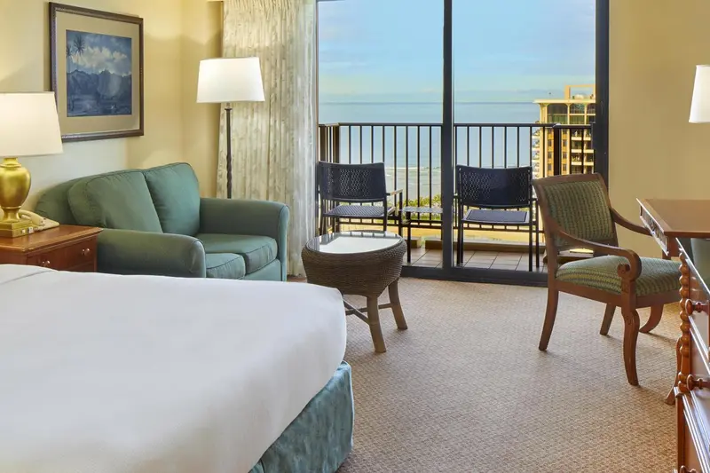 Une chambre lumineuse avec un canapé vert et un balcon donnant sur la mer.