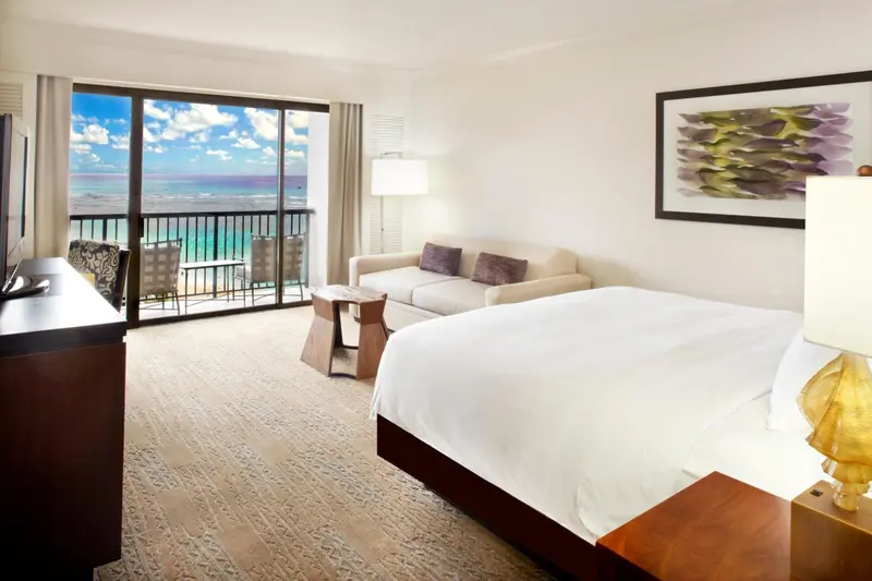 Une chambre lumineuse avec un grand lit et un accès à un balcon avec vue sur la mer.