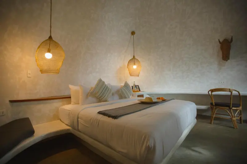 Une chambre lumineuse avec un lit blanc et des suspensions en rotin.