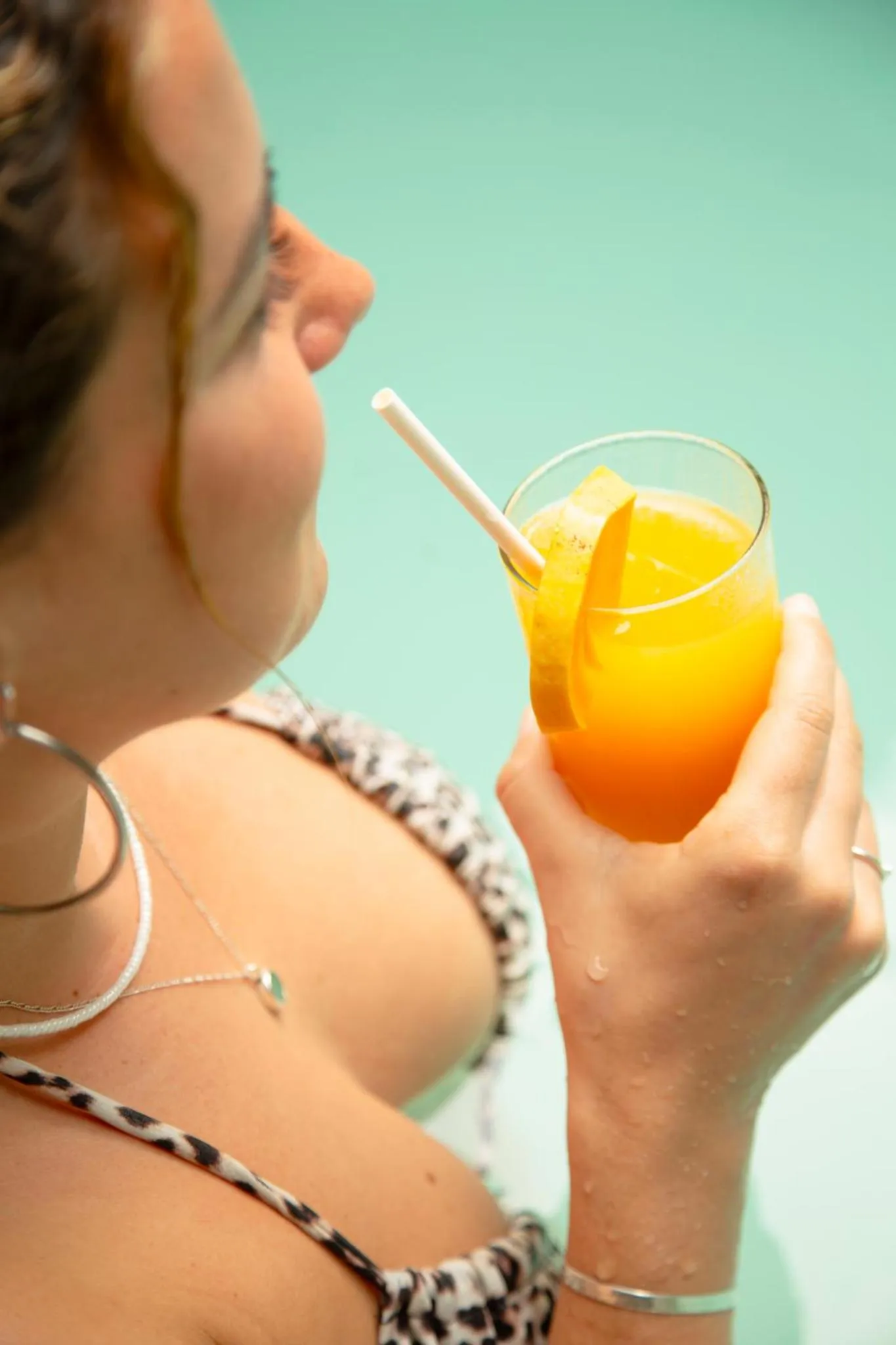 Une personne tient un verre de cocktail coloré au bord d'une piscine.