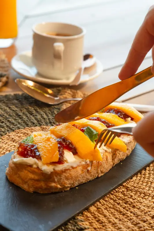 Une tartine de confiture et de fruits frais est préparée sur une table.
