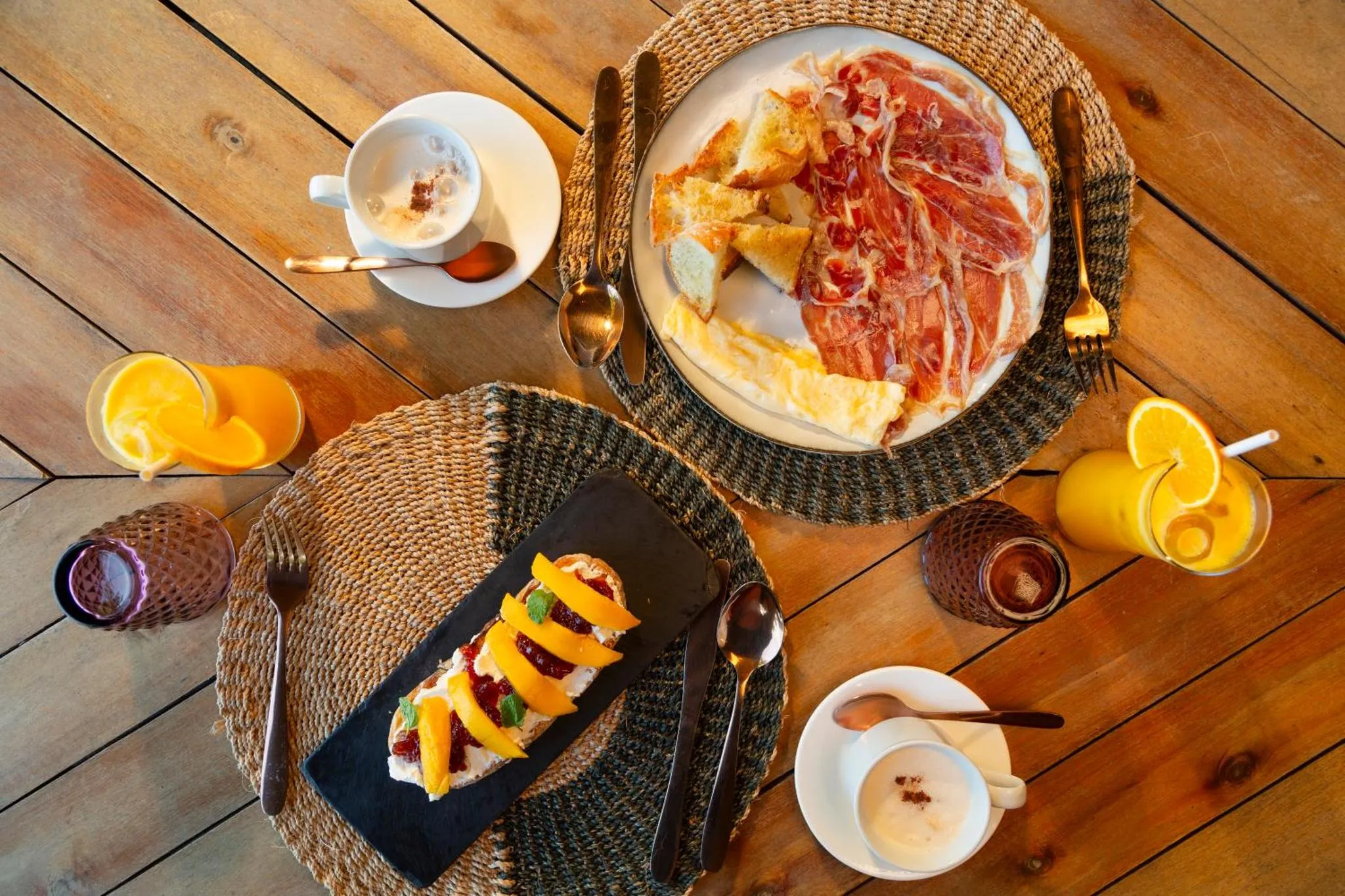 Une table en bois présente un petit-déjeuner avec des œufs, du jambon, du pain et du jus d'orange.