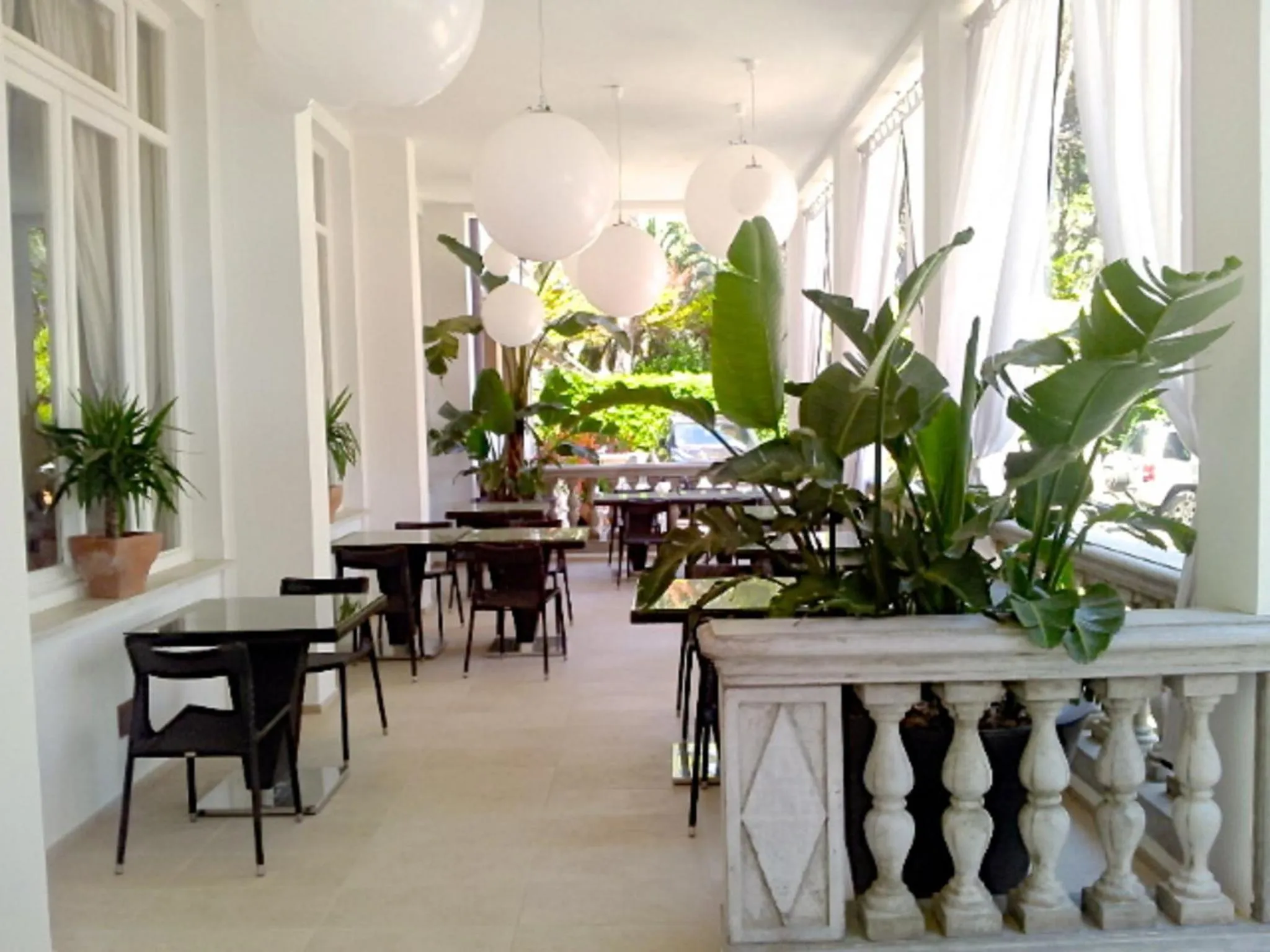 Terrasse ombragée avec tables et chaises, entourée de plantes vertes.