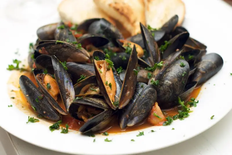 Assiette de moules cuisinées, parsemées de persil.