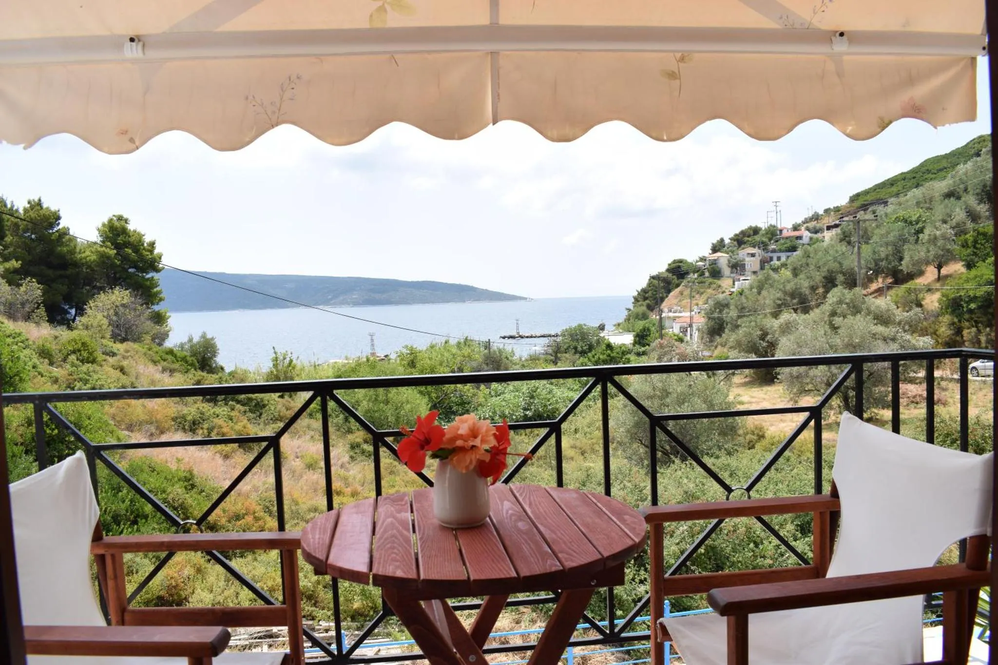 Une table ronde avec des fleurs orne une terrasse avec vue sur la mer et la végétation.