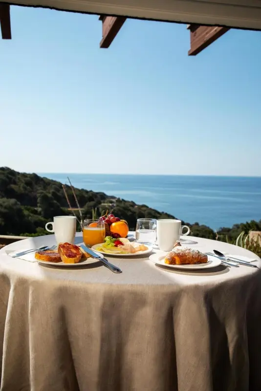 Une table est dressée pour le petit-déjeuner avec vue sur la mer et les collines.