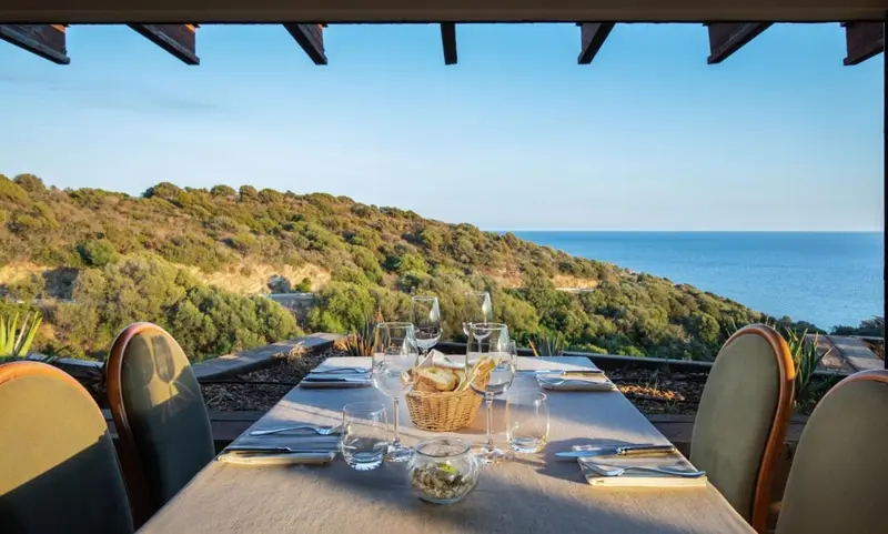 Une table dressée pour un repas en extérieur offre une vue sur la côte et la végétation environnante.