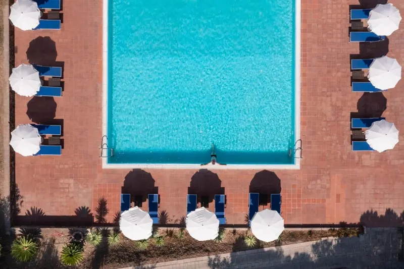 Vue aérienne d'une piscine rectangulaire entourée de transats blancs sous des parasols.