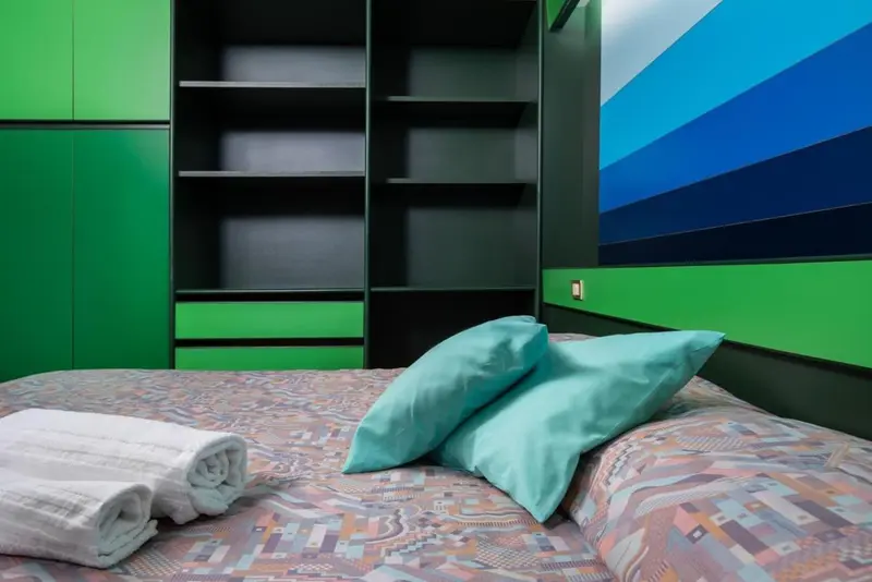 Un lit recouvert d'une couverture colorée avec des oreillers turquoise et une serviette blanche.