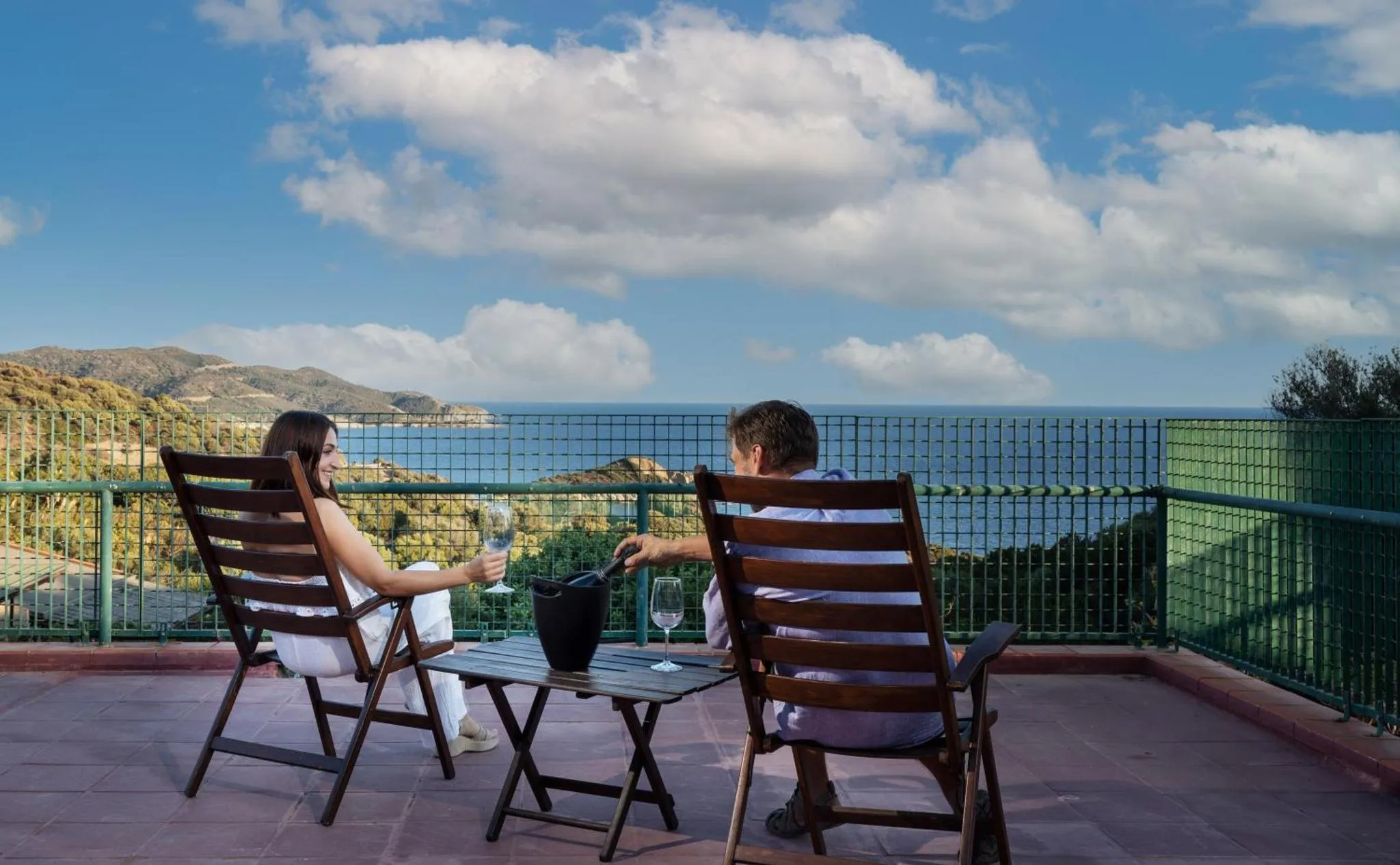 Un couple se détend sur une terrasse avec vue sur la mer et les montagnes.
