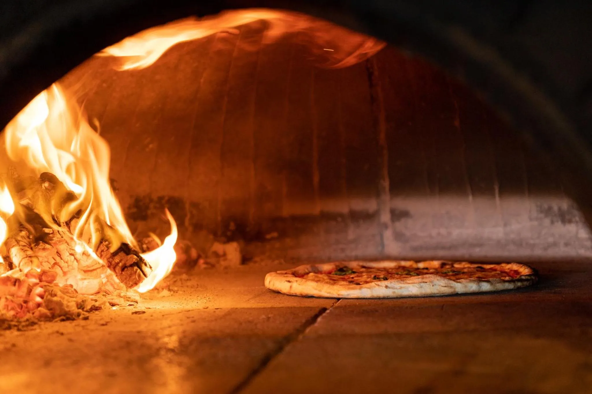 Une pizza cuit dans un four à bois allumé.