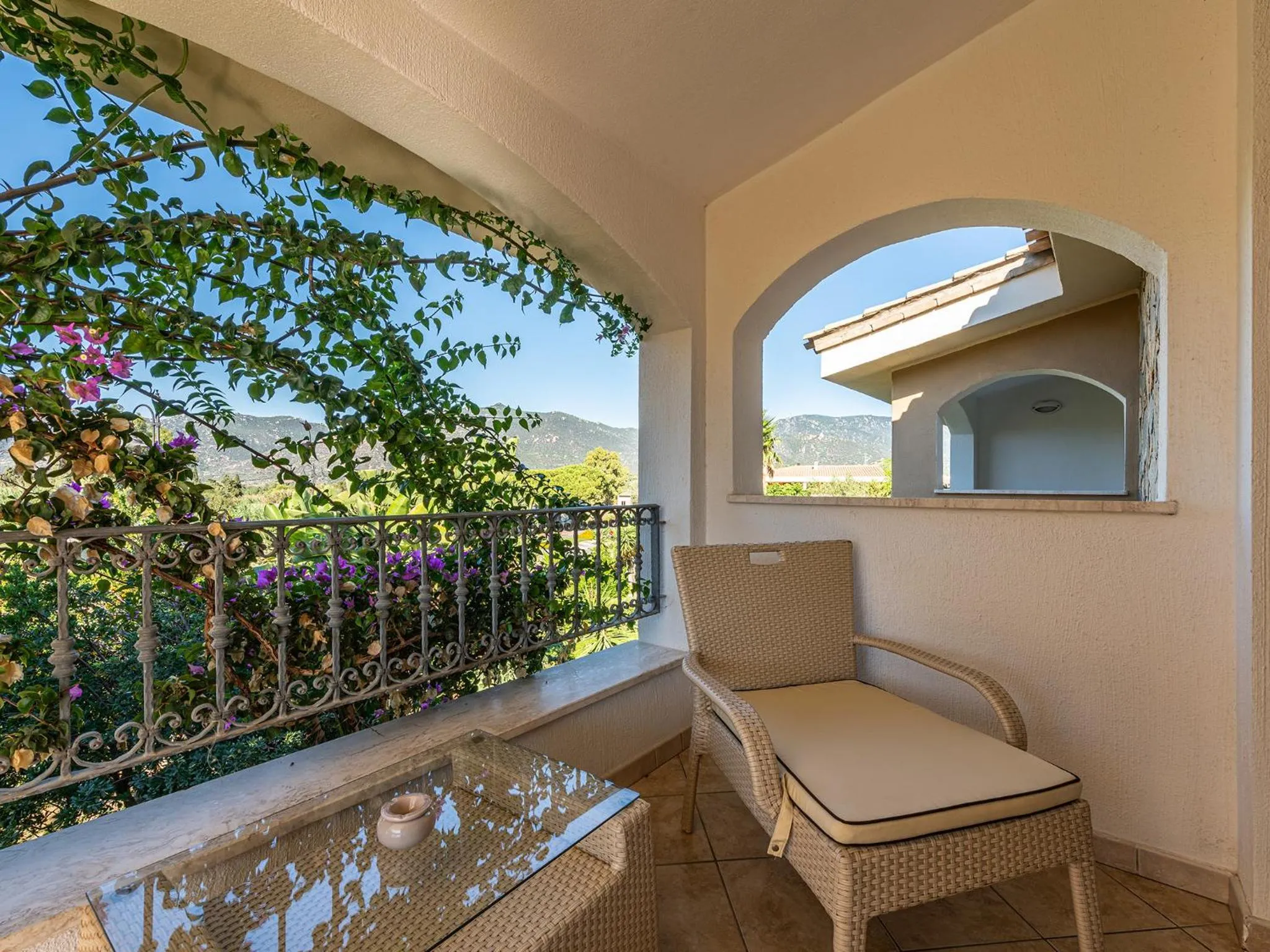 Terrasse ombragée avec mobilier en rotin et vue sur la végétation.