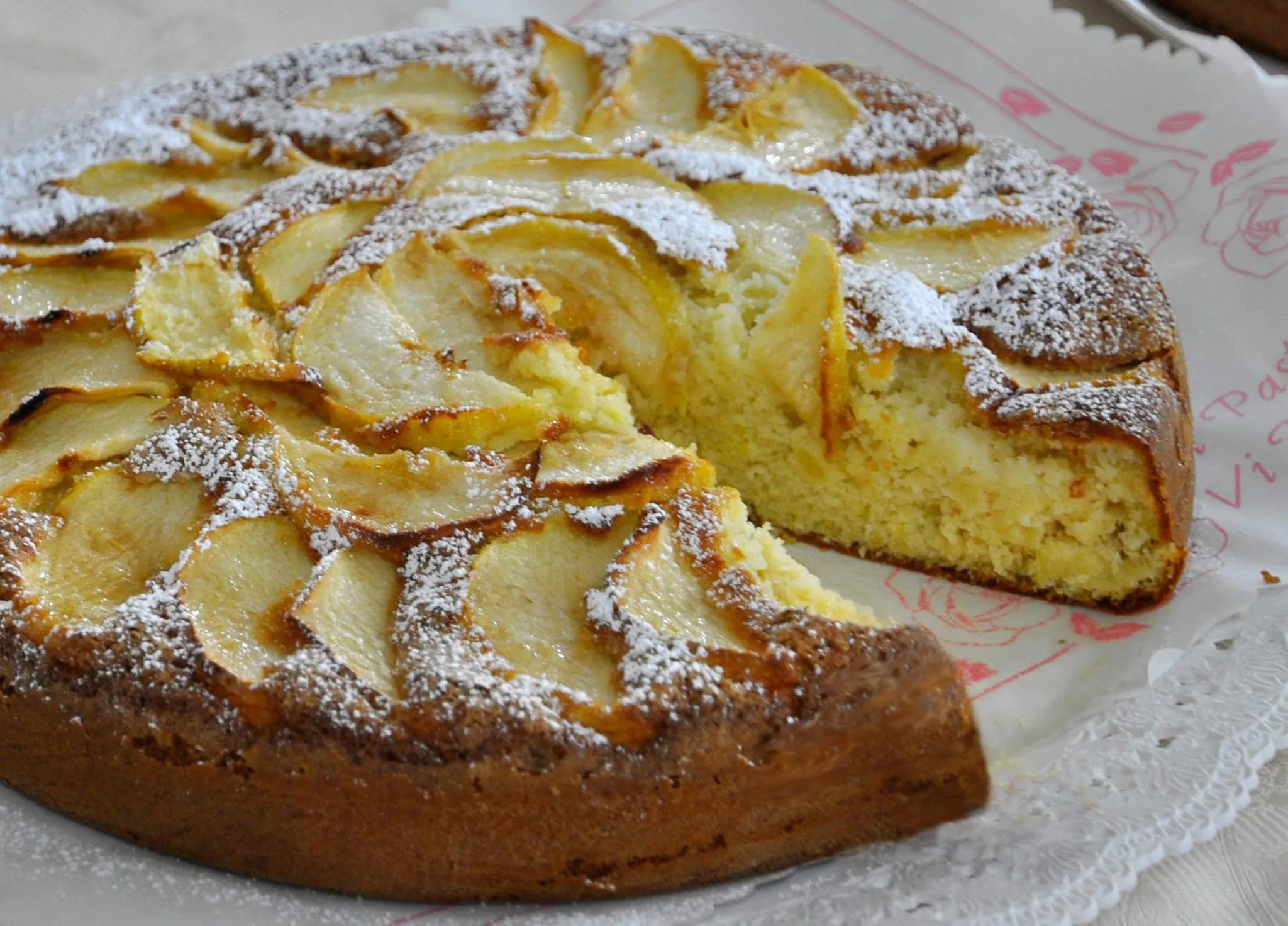 Une tarte aux pommes recouverte de sucre glace est présentée sur une nappe à motifs.