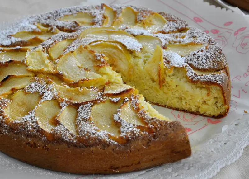 Une tarte aux pommes recouverte de sucre glace est présentée sur une nappe à motifs.